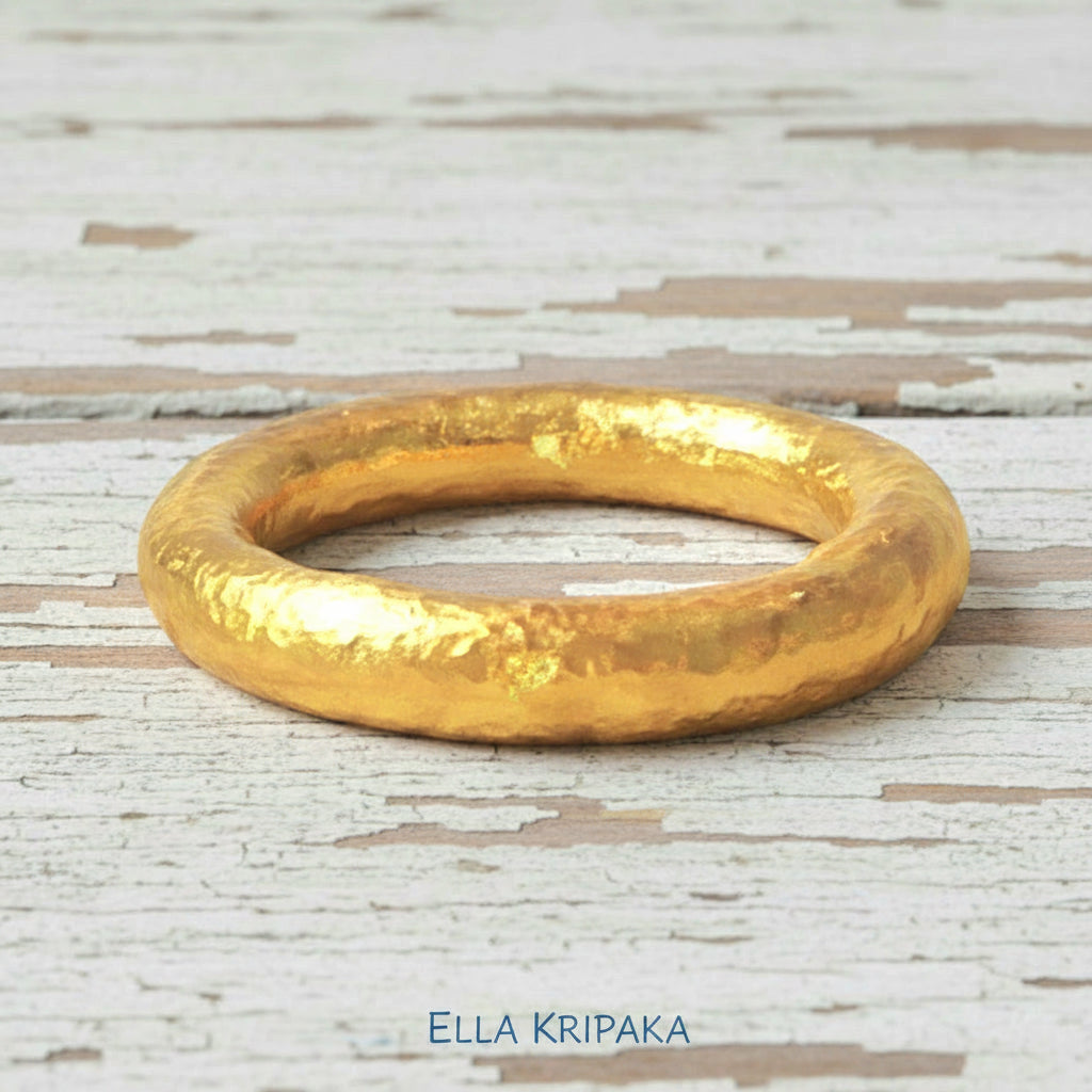 Hammered 24k gold rounded textured ring band on a white old wooden surface with 'Ella Kripaka' branding