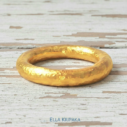 Hammered 24k gold rounded textured ring band on a white old wooden surface with 'Ella Kripaka' branding