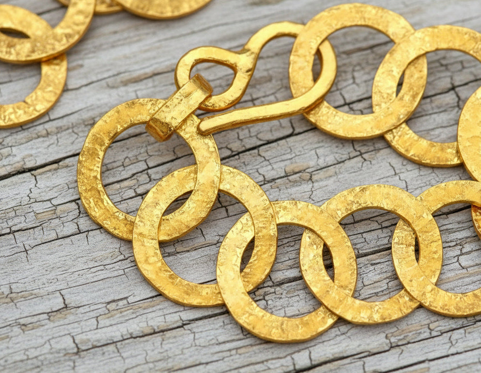 22k gold hammered chain necklace with thick hook clasp on a grey wooden background, artist-jeweler's name 'Ella Kripaka' branding
