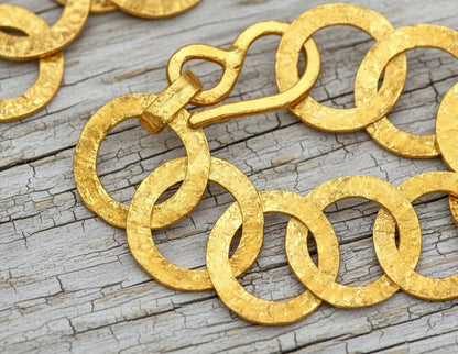 22k gold hammered chain necklace with thick hook clasp on a grey wooden background, artist-jeweler's name 'Ella Kripaka' branding