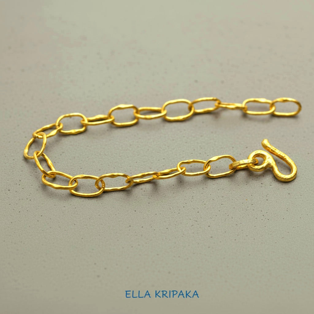 22k gold hammered chain bracelet with thick hook clasp on grey concrete background, artist-jeweler's name 'Ella Kripaka' branding