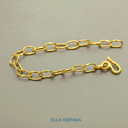 22k gold hammered chain bracelet with thick hook clasp on grey concrete background, artist-jeweler's name 'Ella Kripaka' branding