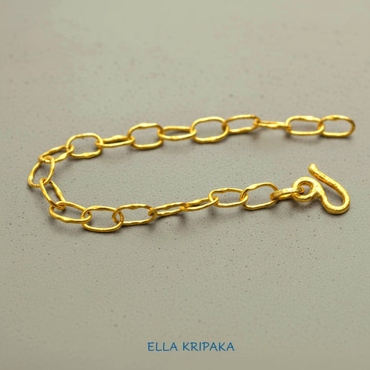 22k gold hammered chain bracelet with thick hook clasp on grey concrete background, artist-jeweler's name 'Ella Kripaka' branding