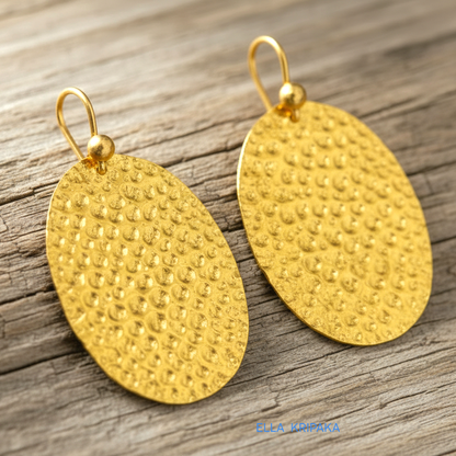 Organic 24k 9999 gold hammered oval earrings with shiny gold textures are on old wooden background, artist-jeweler's name 'Ella Kripaka'