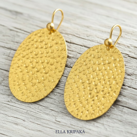 24k gold hammered oval earrings with shiny textured reliefs are on light grey old wooden background, artist-jeweler's name 'Ella Kripaka'