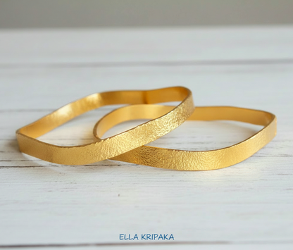 Organic 24k 9999 gold two hammered uneven bangles thick bracelets on white wooden surface, artist-jeweler 'Ella Kripaka'