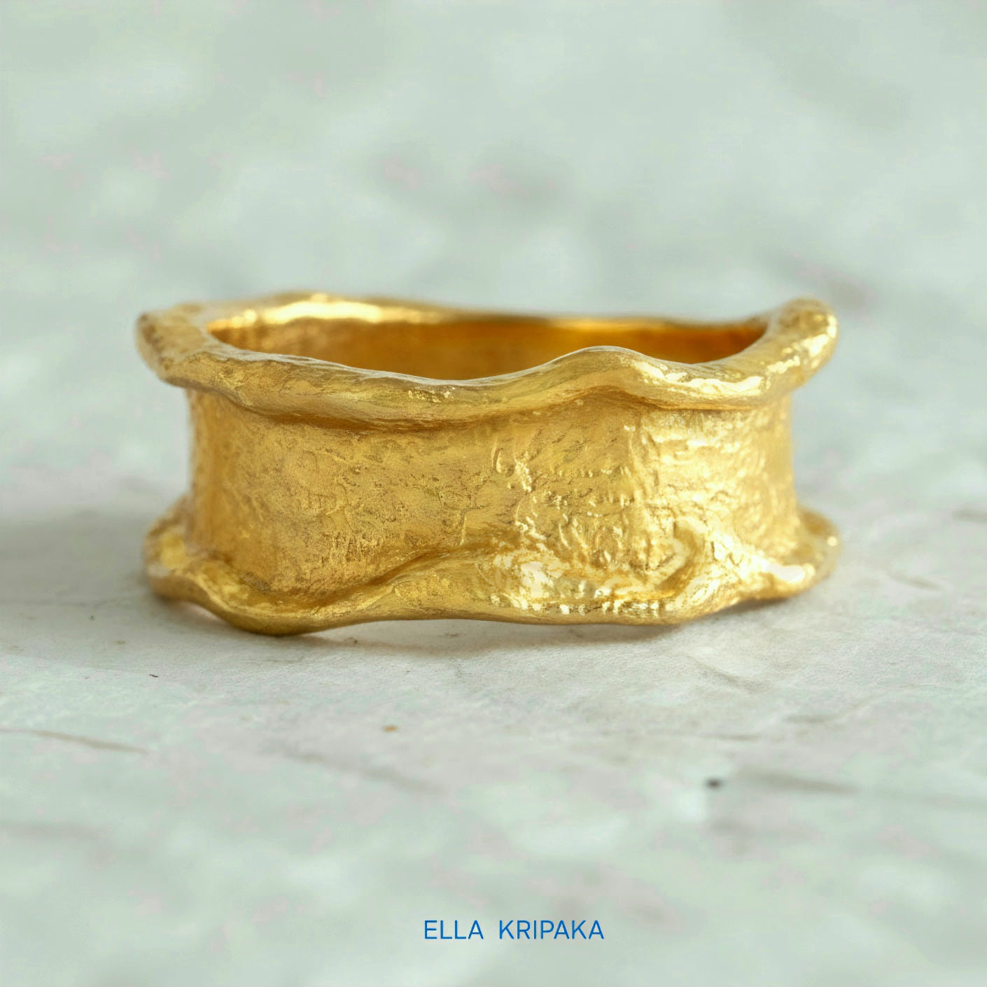 Organic 24k gold hammered ring with textured surface and uneven edges on a white craft  paper background, branded 'Ella Kripaka'