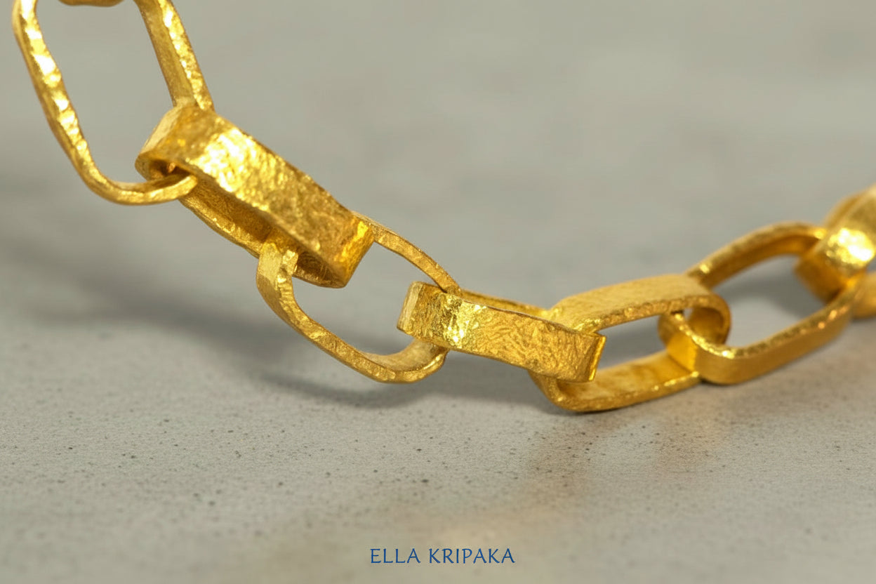 Hammered 24k chain necklace Ancient Rome style on a grey concrete background, branding artist-jeweler name 'Ella Kripaka'
