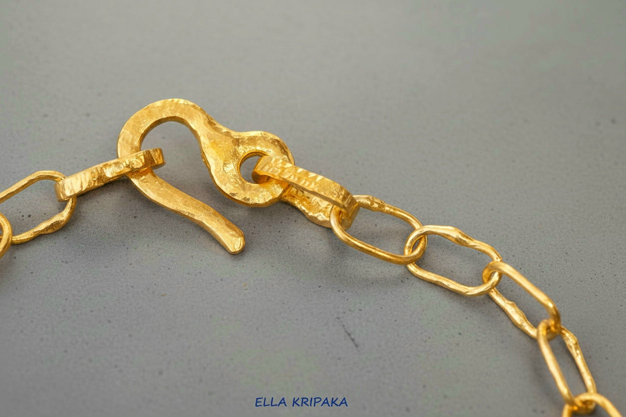 22k gold hammered chain with thick hook clasp on grey concrete background, artist-jeweler's name 'Ella Kripaka' branding