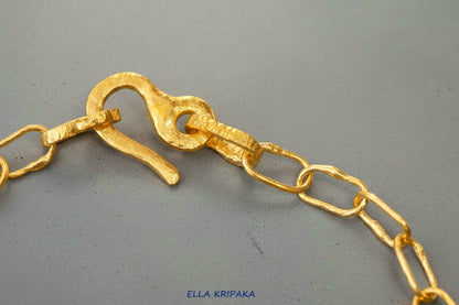 22k gold hammered chain with thick hook clasp on grey concrete background, artist-jeweler's name 'Ella Kripaka' branding