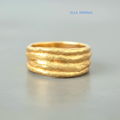 Organic hammered 24k 9999 gold convex ring with uneven thick edges on grey surface, artist-jeweler's name 'Ella Kripaka' is written in picture