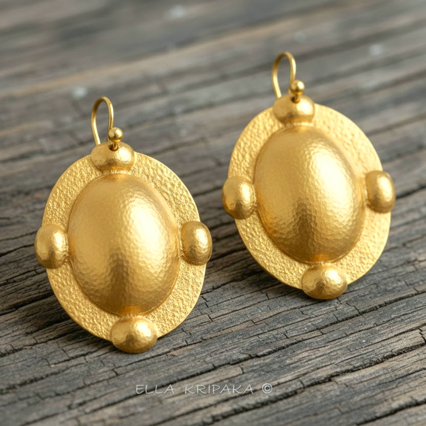 Hammered 24k gold, pure 9999 gold Byzantine convex ovals earrings with shiny forged gold textures on old wooden surface, artist-jeweler 'Ella Kripaka' branding