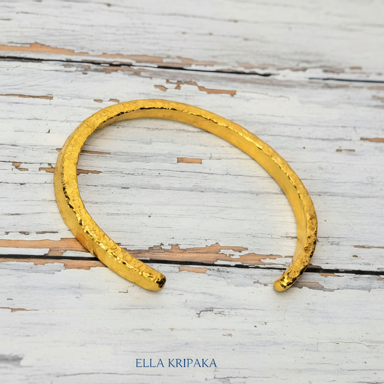Hammered 24k 9999 gold cuff thick bracelet Ancient Rome style on an old white wooden background, artist-jeweler name 'Ella Kripaka' branding