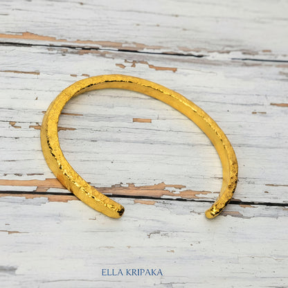 Hammered 24k 9999 gold cuff thick bracelet Ancient Rome style on an old white wooden background, artist-jeweler name 'Ella Kripaka' branding