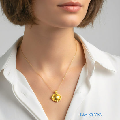 Hammered 24k gold convex Byzantine pendant with chain worn by a woman and with a white shirt background with 'Ella Kripaka' branding