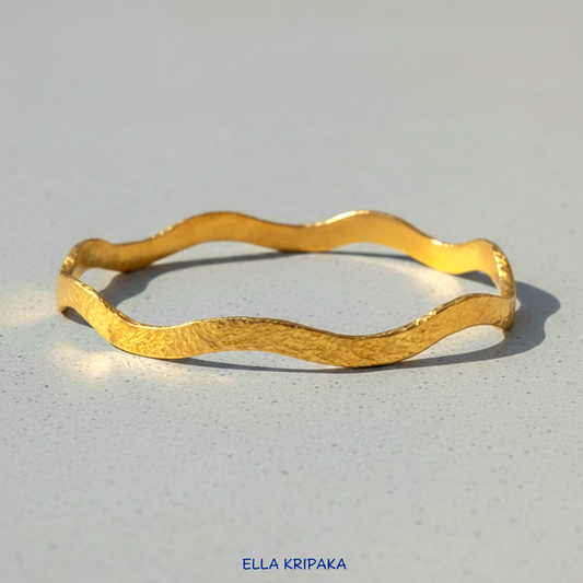 24k gold hammered bracelet bangle with wavy design on grey concrete background, branded 'Ella Kripaka'