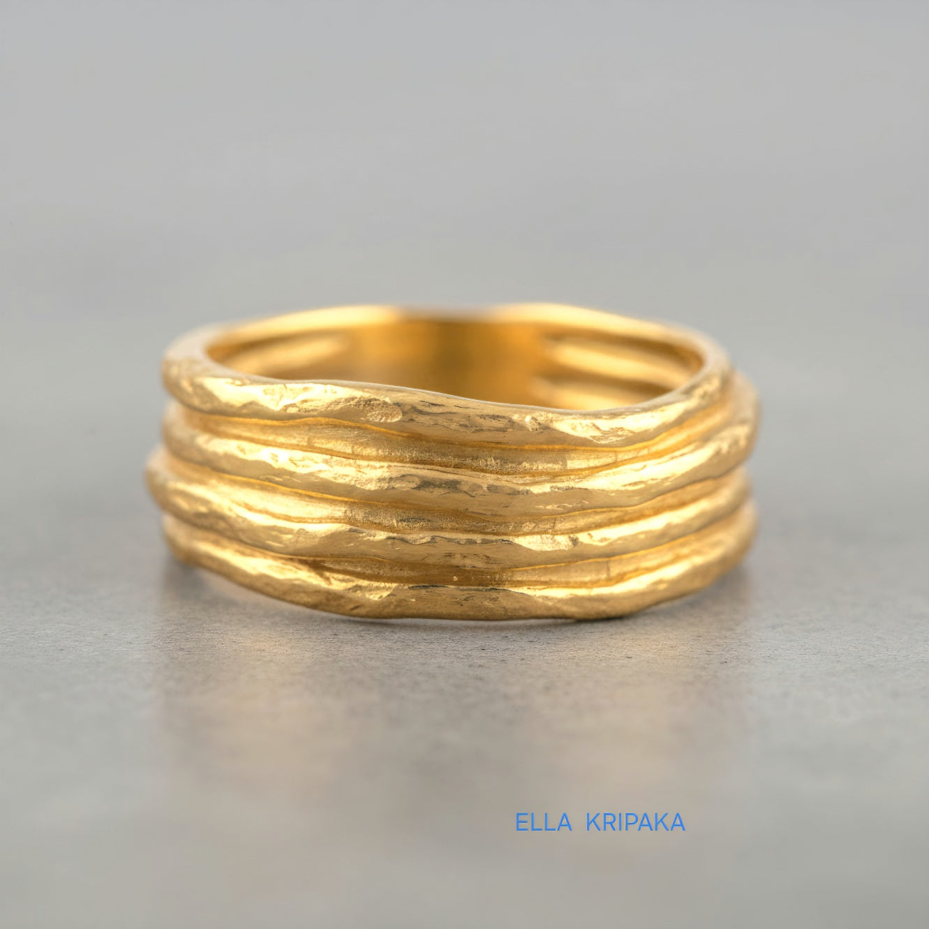 Organic hammered 24k 9999 gold convex ring with uneven thick edges on grey surface, artist-jeweler's name 'Ella Kripaka' is written in picture