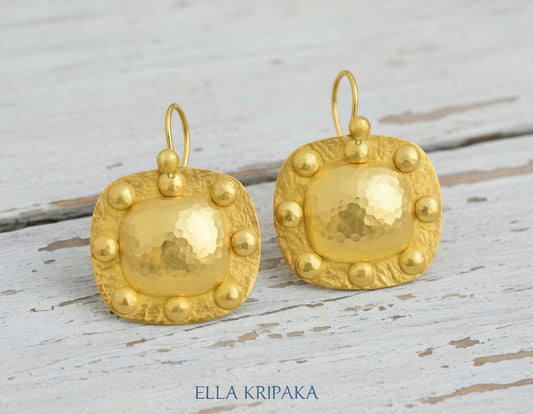 Solid 24k 9999 gold hammered Byzantine convex square earrings with hook clasps and shiny forged gold textures on old wooden background , artist's name 'ELLA KRIPAKA'