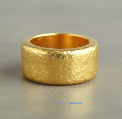 Hammered 24k Gold 9999 gold ring band thick heavy and with textured surface on a grey concrete background, branded 'Ella Kripaka'