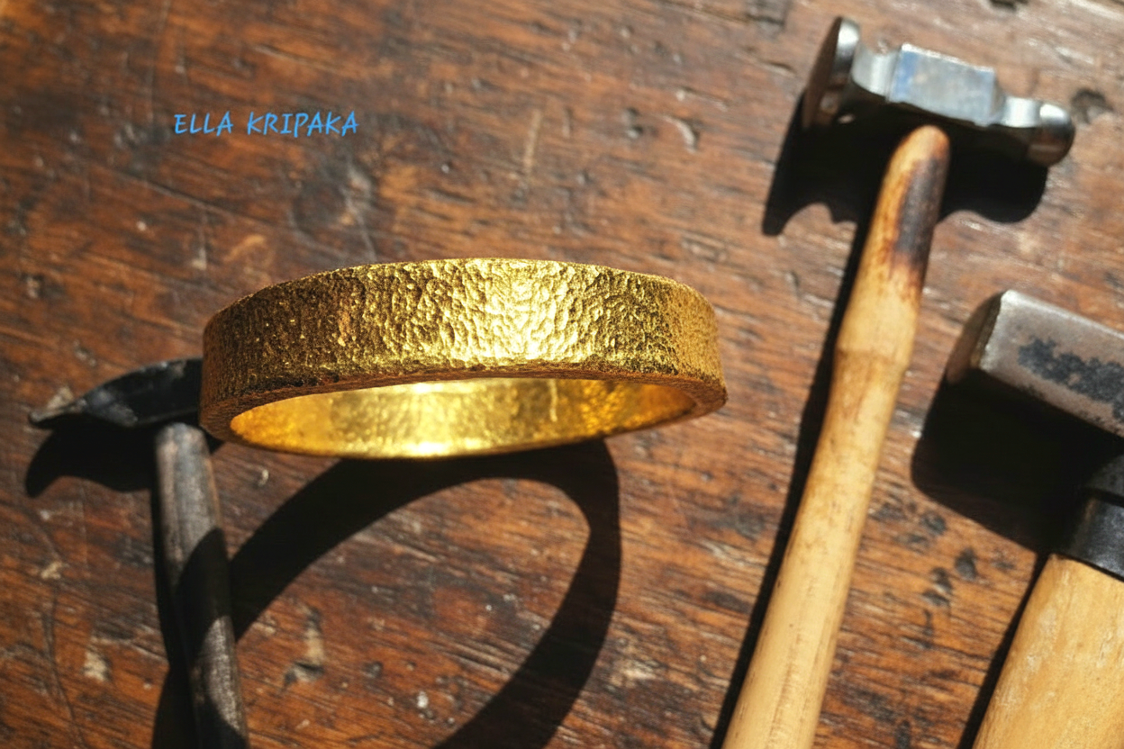 24k gold hammered bangle thick textured bracelet on a dark old jewelry table surface with jewelry tools and hammers, artist's name 'Ella Kripaka' branding