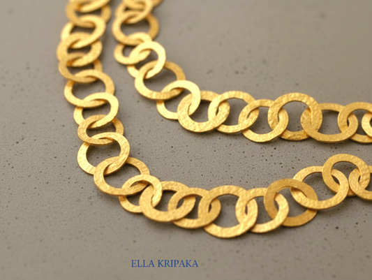 22k gold hammered chain necklace with different links on a grey concrete surface, and with 'Ella Kripaka' branding