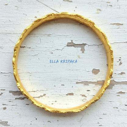Hammered 22k gold organic textured bangle bracelet with uneven edges on old white wooden surface with 'Ella Kripaka' branding