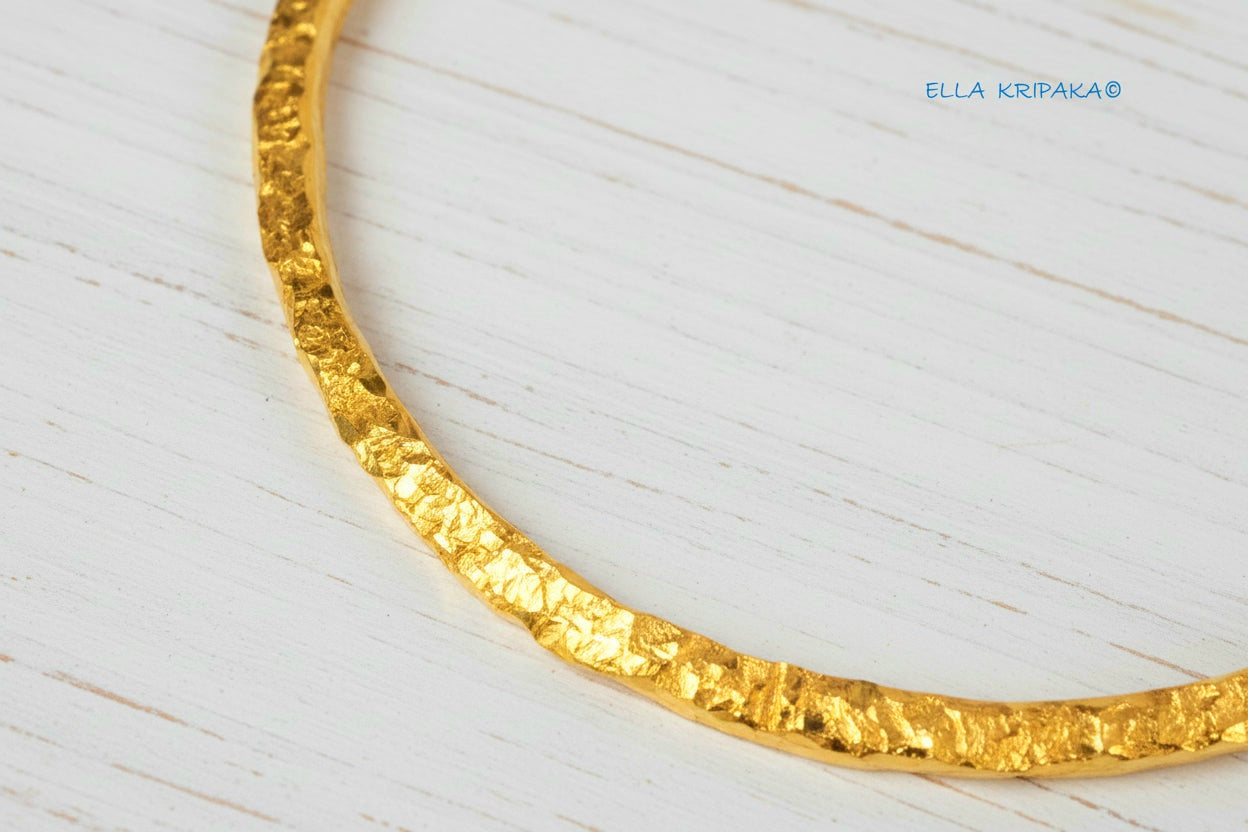 Organic 24k gold textured bangle thick bracelet with uneven edges and on a white wooden background, artist-jeweler name 'Ella Kripaka'