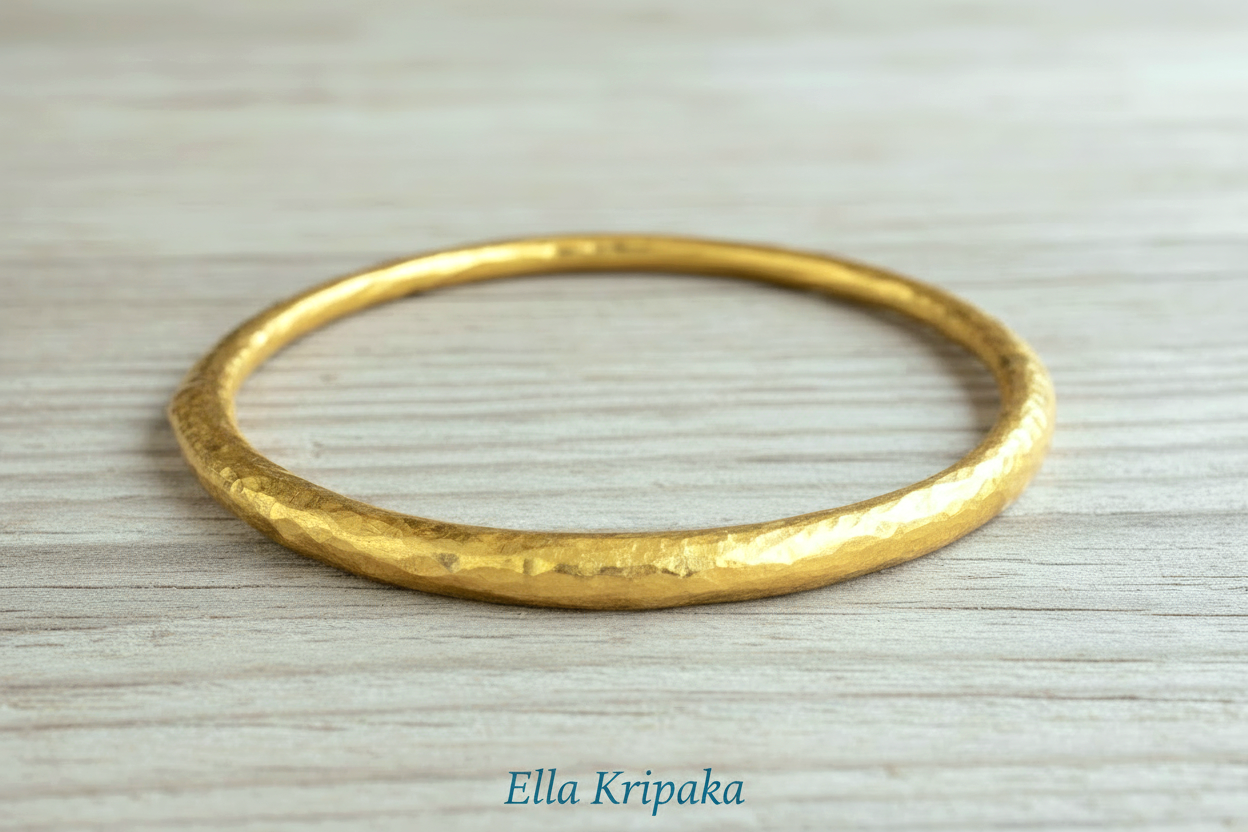 Hammered 24k 9999 gold bangle thick bracelet Ancient Rome style on a wooden background, branding artist-jeweler name 'Ella Kripaka'