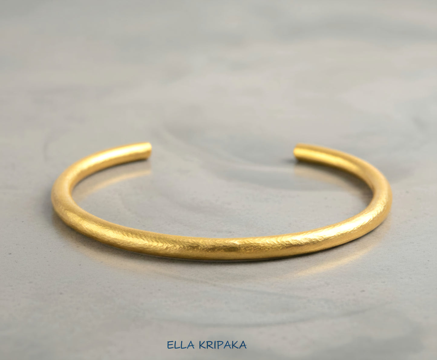 Hammered 24k 9999 gold cuff thick bracelet Ancient Rome style on a grey background, artist-jeweler name 'Ella Kripaka' branding