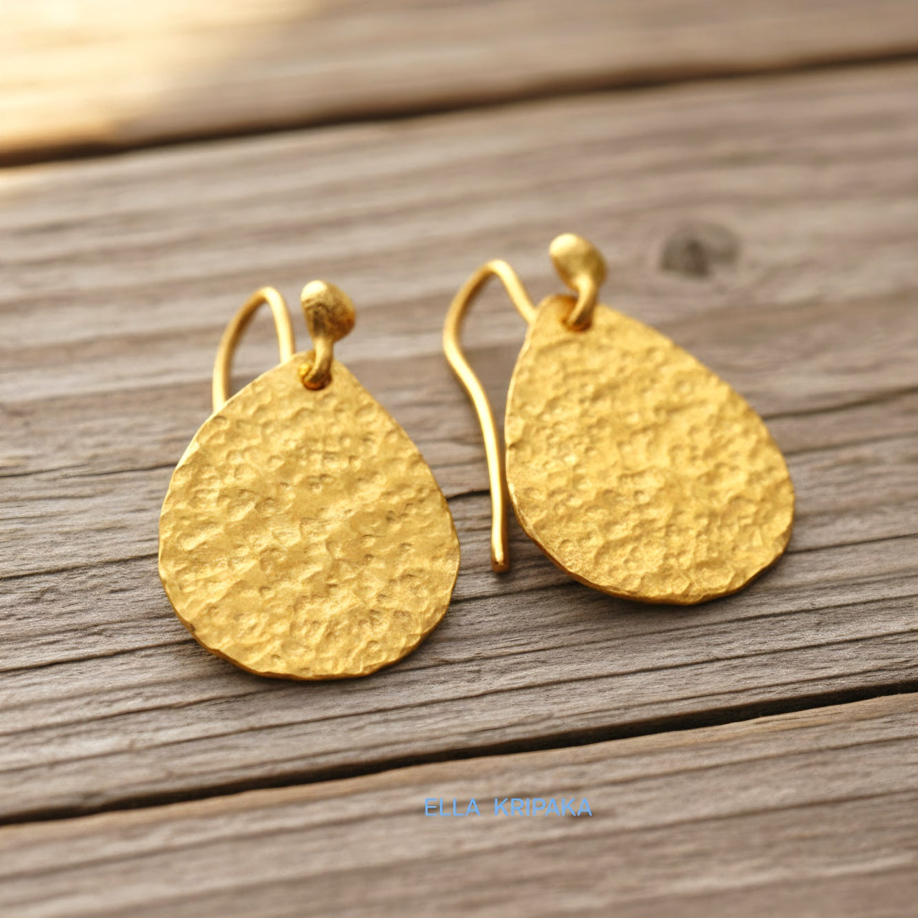 Hammered 24k gold, pure 9999 gold drop earrings with shiny forged gold textures on old wooden surface, artist-jeweler 'Ella Kripaka' branding