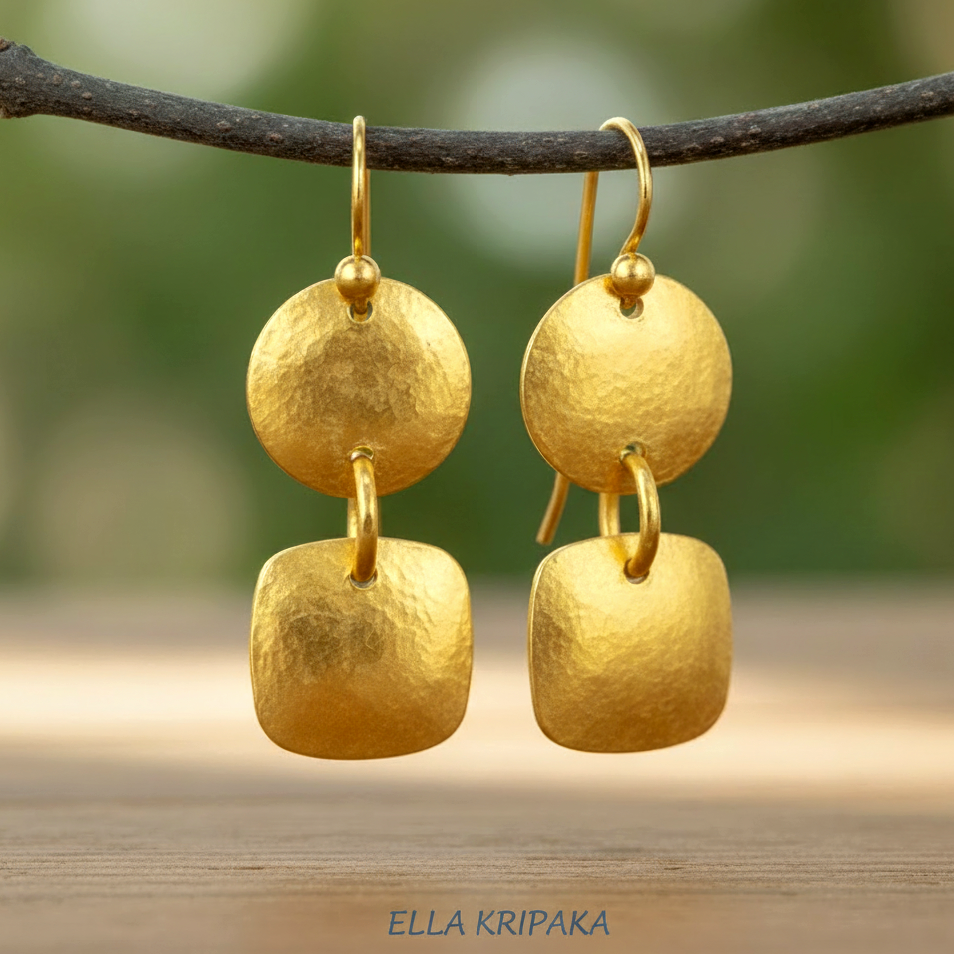 Hammered 24k gold dangling earrings, convex disks and squares, are hanging on a dark branch with a blurred natural background, branding artist-jeweler 'Ella Kripaka'