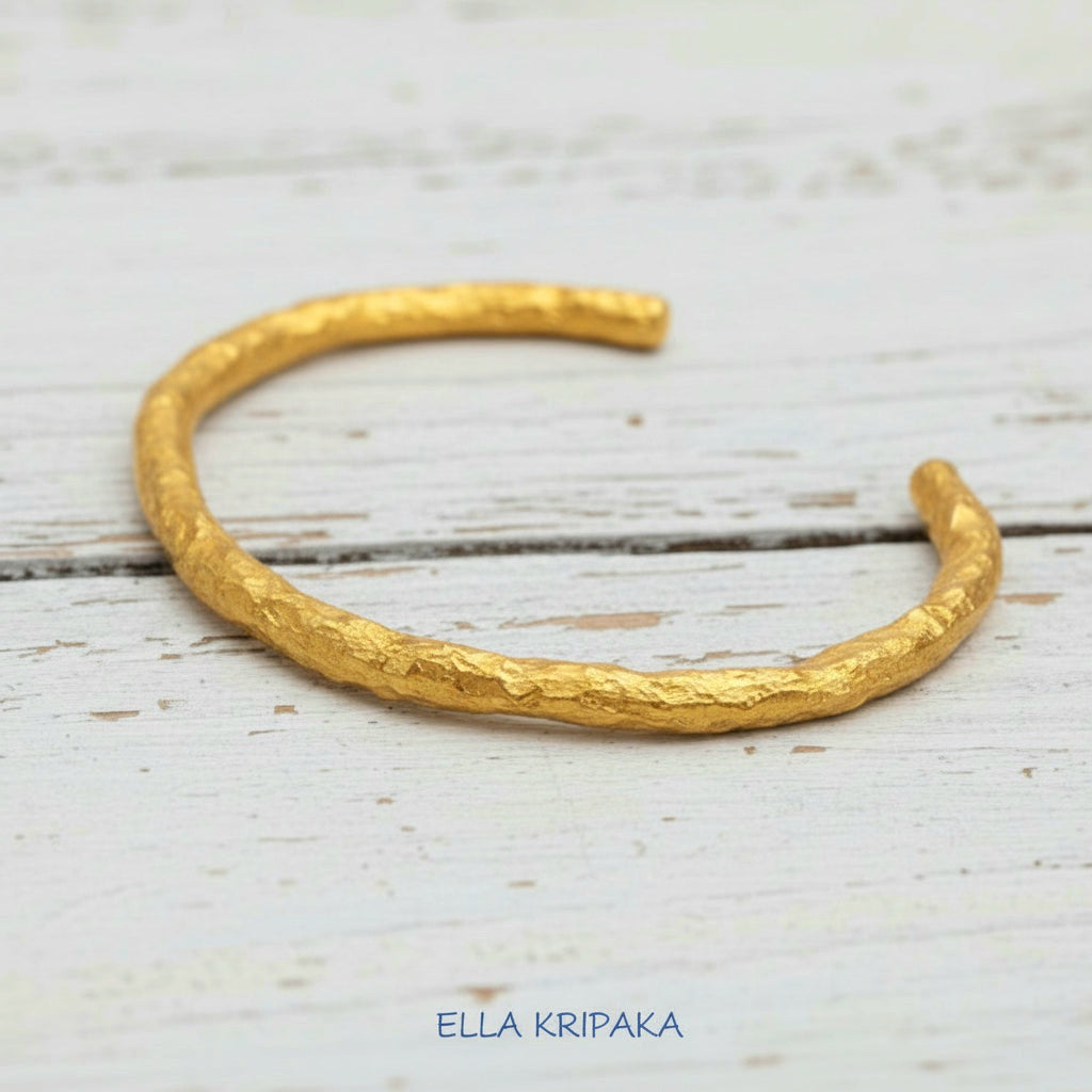 Organic hammered 24k 9999 gold bracelet uneven cuff on a old white old wooden background, branding artist-jeweler name 'Ella Kripaka'