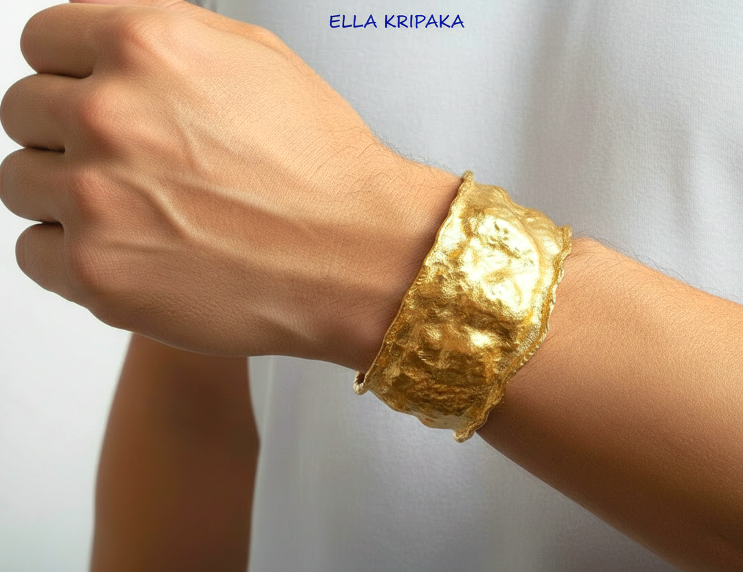 Organic 24k gold hammered bracelet cuff with a textured surface on a man's wrist and with blurred light background, branded 'Ella Kripaka'