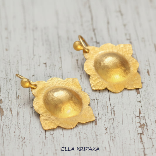 24k gold hammered baroque convex earrings with shiny gold textures are on white old wooden background, artist-jeweler's name 'Ella Kripaka'
