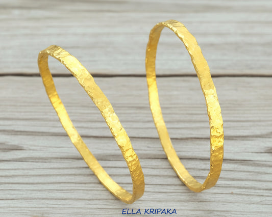 Organic hammered 24k 9999 Gold thick two bangles uneven bracelets on a wooden background, artist's name 'Ella Kripaka' branding
