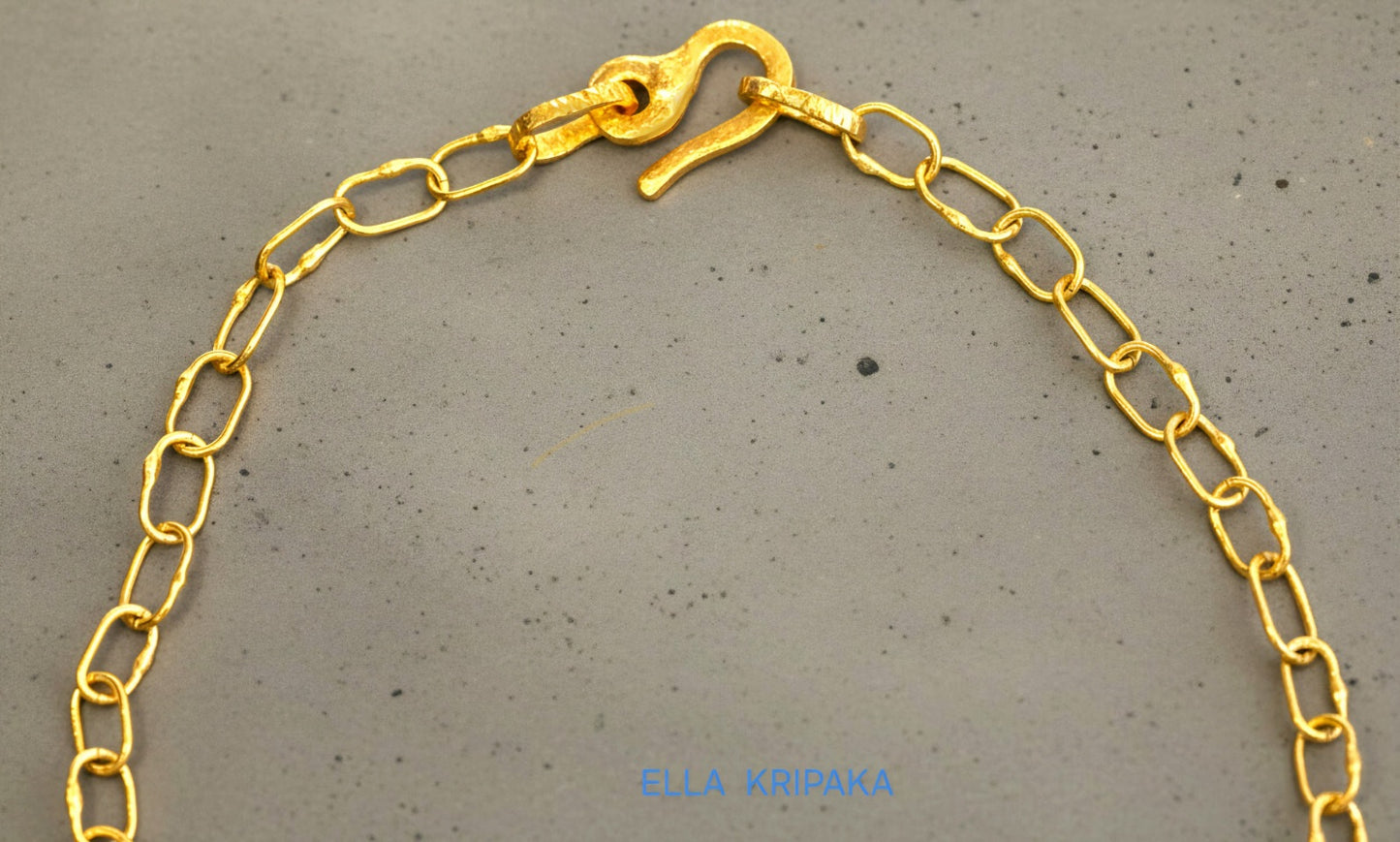 22k gold hammered chain necklace with thick hook clasp on grey concrete background, artist-jeweler's name 'Ella Kripaka' branding