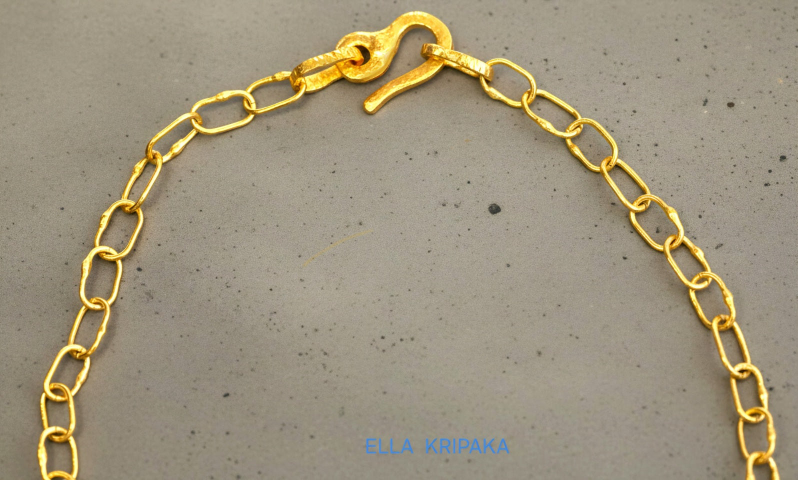 22k gold hammered chain necklace with thick hook clasp on grey concrete background, artist-jeweler's name 'Ella Kripaka' branding