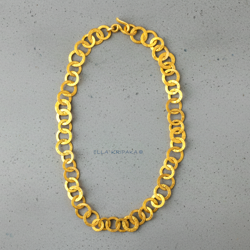 22k gold hammered chain necklace with different links and with thick hook clasp on a grey concrete surface, and with 'Ella Kripaka' branding