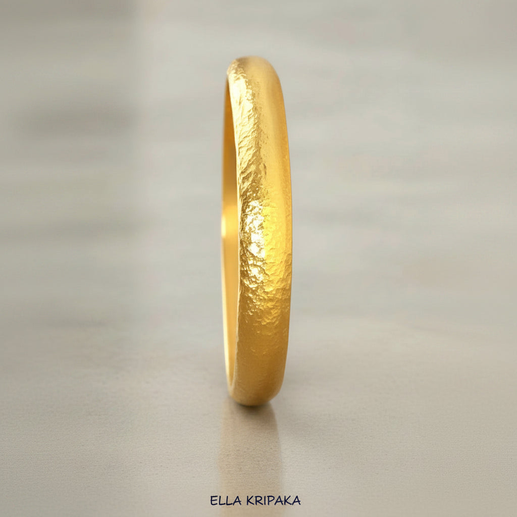 Hammered 24k gold bangle thick bracelet with rounded edges on grey concrete background, and artist-jeweler 'Ella Kripaka' branding