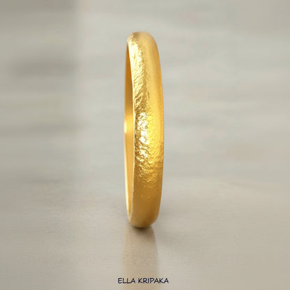 Hammered 24k gold bangle thick bracelet with rounded edges on grey concrete background, and artist-jeweler 'Ella Kripaka' branding