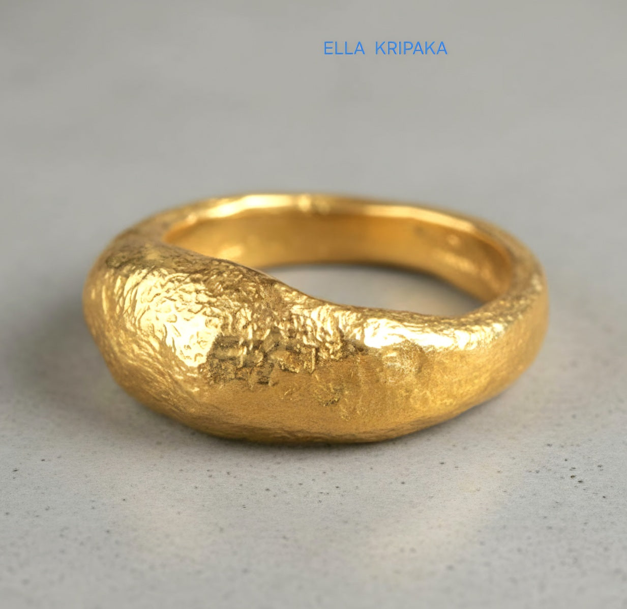 Hammered organic 24k Gold 9999 gold uneven signet thick ring with textured gold on a grey concrete background, branded 'Ella Kripaka'