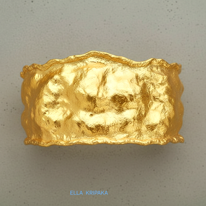 Organic 24k gold hammered bracelet cuff with a textured surface on a grey concrete background, branded 'Ella Kripaka'