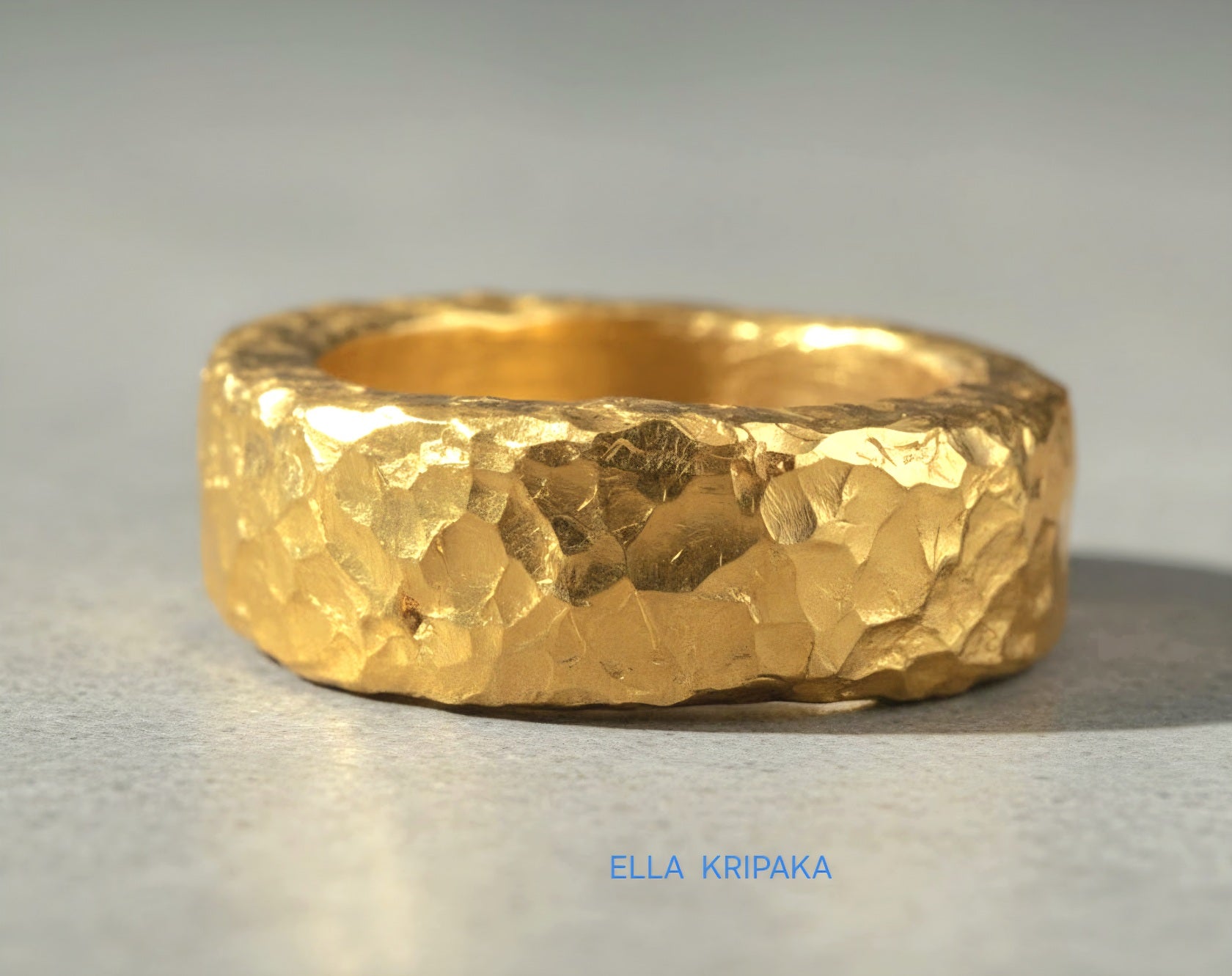 Hammered 24k 9999 Gold thick uneven ring organic with a textured gold surface on a grey concrete background, branded 'Ella Kripaka'