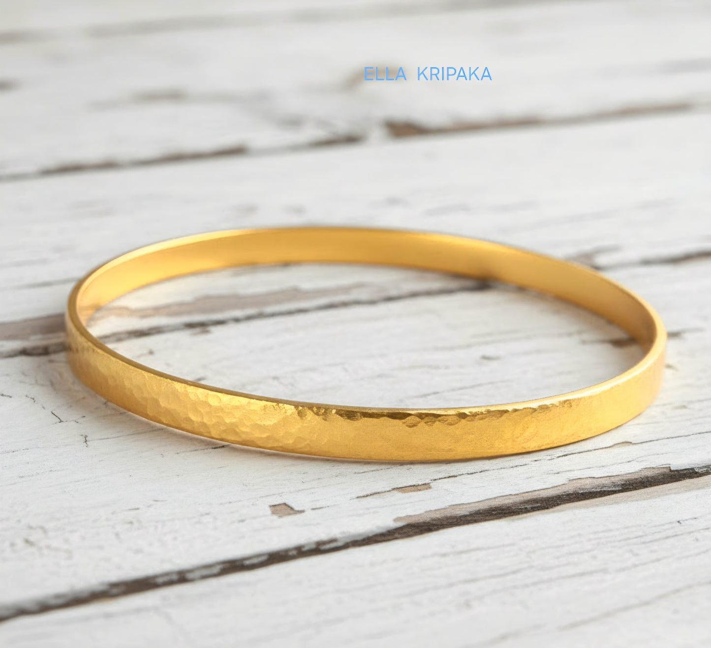24k 9999 gold hammered Ancient Rome style bracelet bangle on white rustic wooden surface, indicating it is a custom-made jewelry with creator's name 'Ella Kripaka'