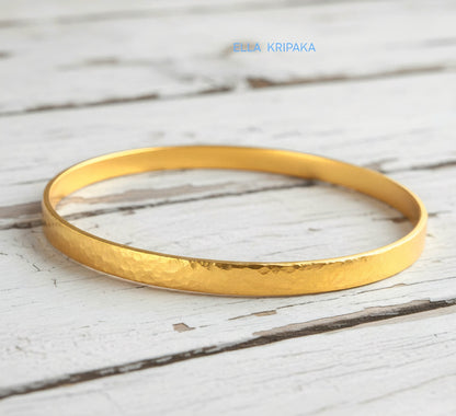 24k 9999 gold hammered Ancient Rome style bracelet bangle on white rustic wooden surface, indicating it is a custom-made jewelry with creator's name 'Ella Kripaka'