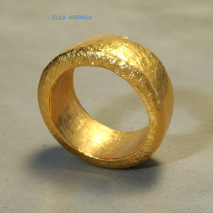 Hammered 24k Gold 9999 gold ring band thick heavy and with textured surface on a grey concrete background, branded 'Ella Kripaka'