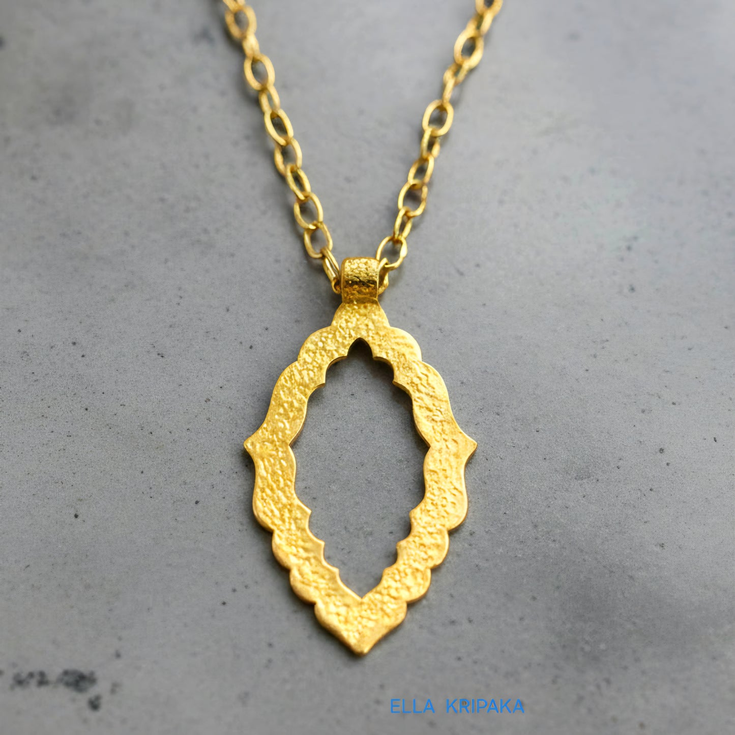 Hammered 24k gold Byzantine ornament pendant with chain on a grey concrete surface with 'Ella Kripaka' branding