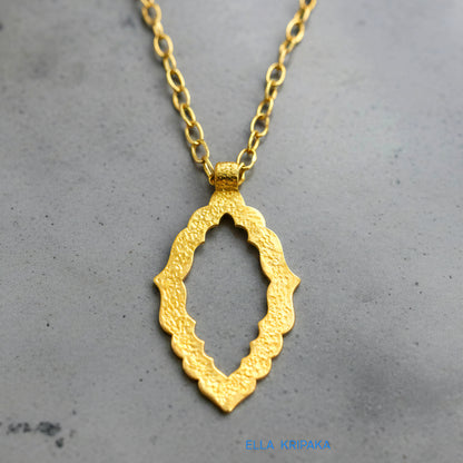 Hammered 24k gold Byzantine ornament pendant with chain on a grey concrete surface with 'Ella Kripaka' branding