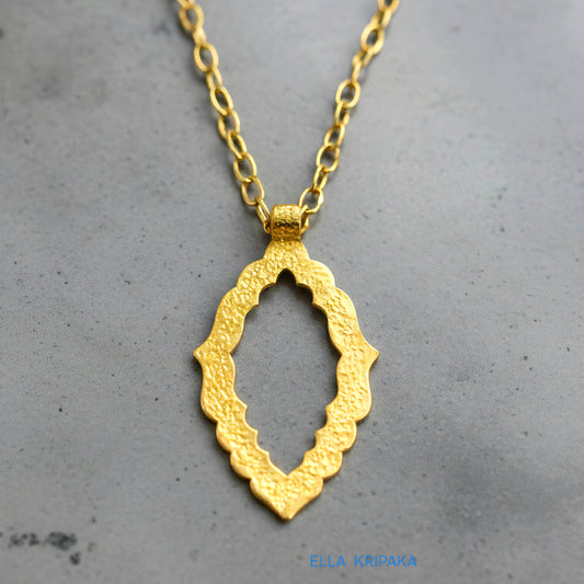 Hammered 24k gold Byzantine ornament pendant with chain on a grey concrete surface with 'Ella Kripaka' branding