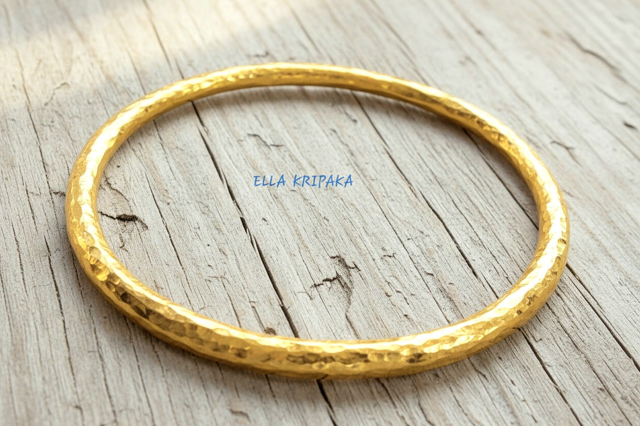Hammered 24k 9999 gold bangle thick bracelet Ancient Rome style on a wooden background, branding artist-jeweler name 'Ella Kripaka'